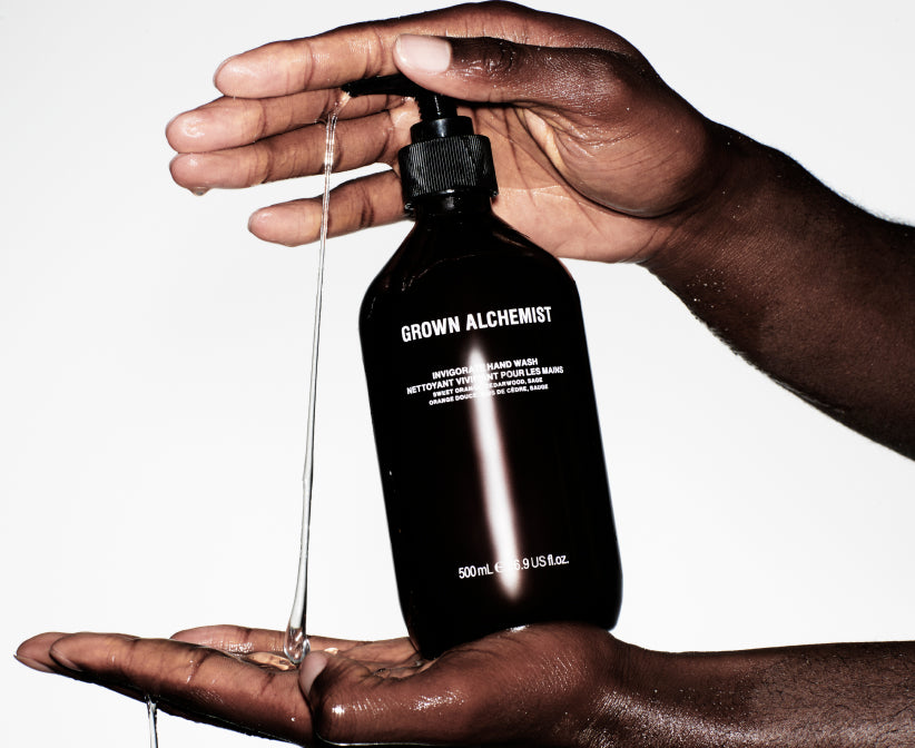 Hand holding a Grown Alchemist bottle with liquid dripping onto another hand against a white background