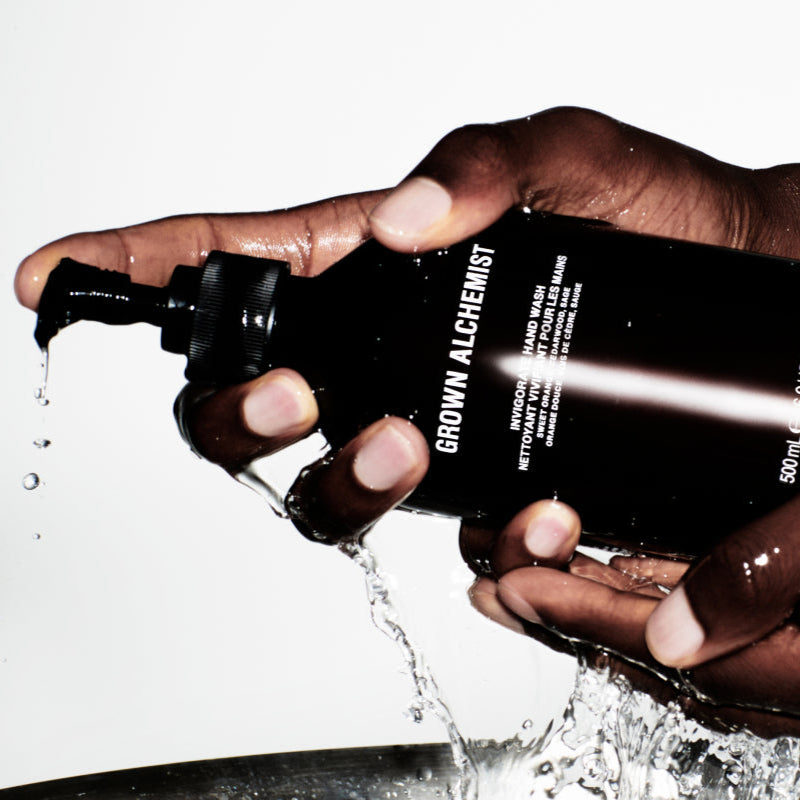 Hand holding a Grown Alchemist bottle with water splashing out, on a white background