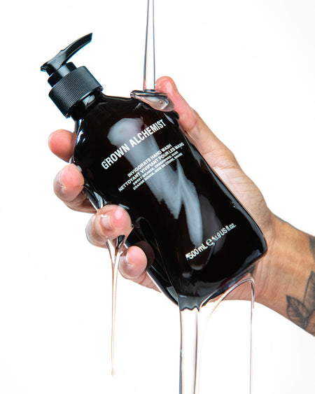 Hand holding a black bottle labeled 'Grown Alchemist' with liquid dripping.