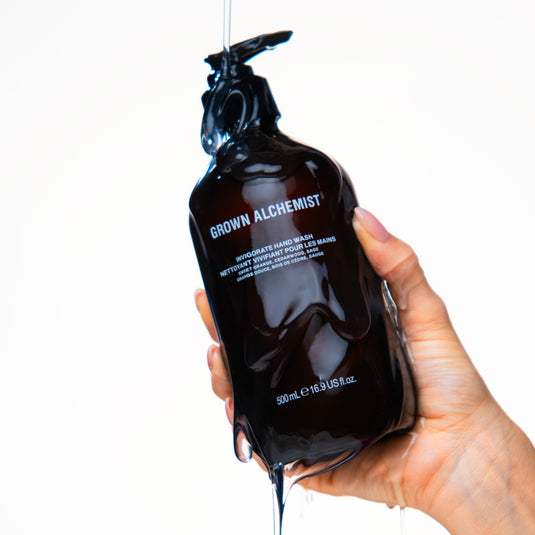 Hand holding a Grown Alchemist black bottle with white text on a white background