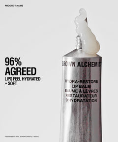 A silver tube of Brown Alchemist Hydra-Restore Lip Balm with a white balm smear at the tip, shown on a light gray background with promotional text on the left.