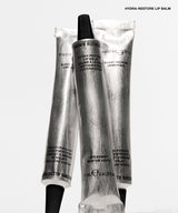 Three silver squeeze tubes of Almers Hydra-Restore Lip Balm with black caps, arranged vertically on a clean white background. The text 'HYDRA-RESTORE LIP BALM' is printed in black at the top right.