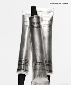 Three silver squeeze tubes of Almers Hydra-Restore Lip Balm with black caps, arranged vertically on a clean white background. The text 'HYDRA-RESTORE LIP BALM' is printed in black at the top right.