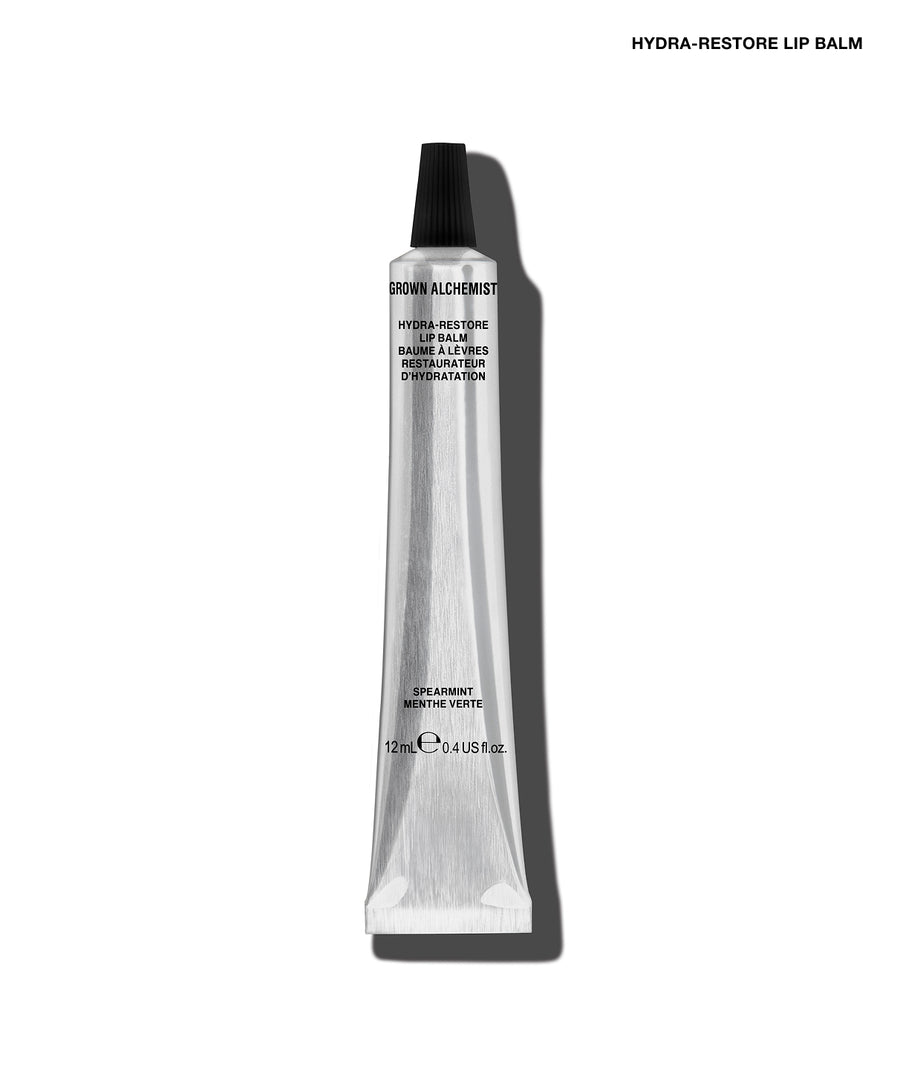A single tube of GROW ALCHEMY Hydra-Restore Lip Balm on a clean white background with a soft shadow. The tube is metallic silver with a black cap, and the text 'HYDRA-RESTORE LIP BALM' is printed at the top right.