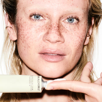 Person holding a skincare product with a close-up of her face showing freckles.