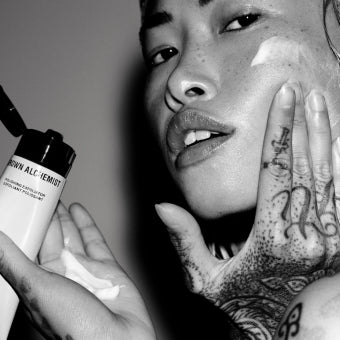 Person applying skincare product with tattooed hands, close-up of face and product.