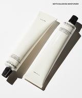 Two white cosmetic tubes, one with a black cap and one without, arranged diagonally on a white background with a text label reading 'MATTE BALANCING MOISTURIZER' at the top.