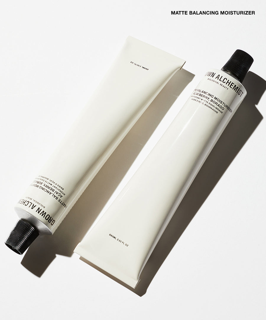 Two white cosmetic tubes, one with a black cap and one without, arranged diagonally on a white background with a text label reading 'MATTE BALANCING MOISTURIZER' at the top.