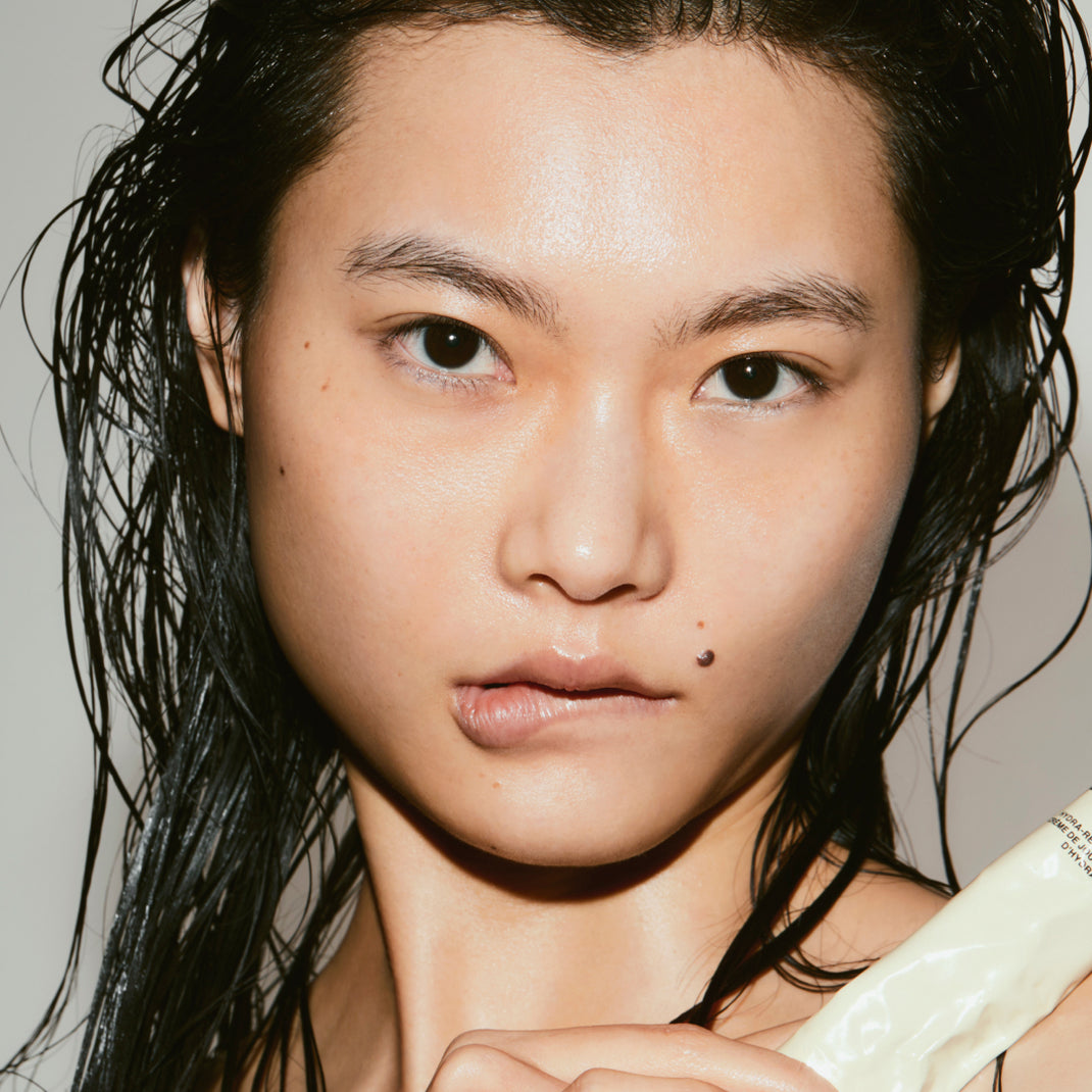 Close-up of a person with wet hair holding Matte Balancing Moisturizer against a neutral background