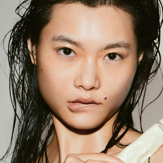 Close-up of a person with wet hair holding Matte Balancing Moisturizer against a neutral background