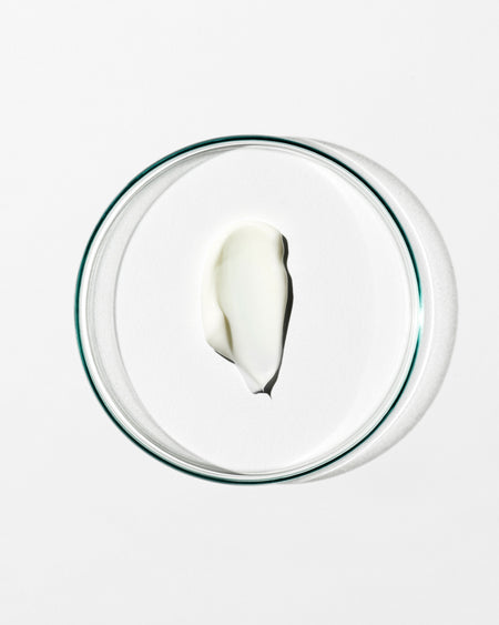 Glass bowl with a small amount of white cream on a white background