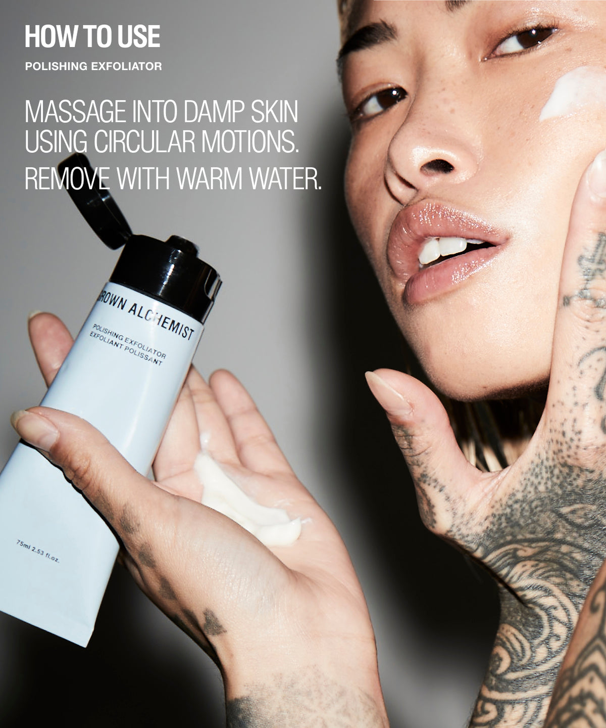 A close-up beauty ad showing a tattooed model applying or holding a tube of Grown Alchemist polishing exfoliator, with text on the left explaining how to use the product. The background is a dark gray studio setting.