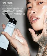 A close-up beauty ad showing a tattooed model applying or holding a tube of Grown Alchemist polishing exfoliator, with text on the left explaining how to use the product. The background is a dark gray studio setting.