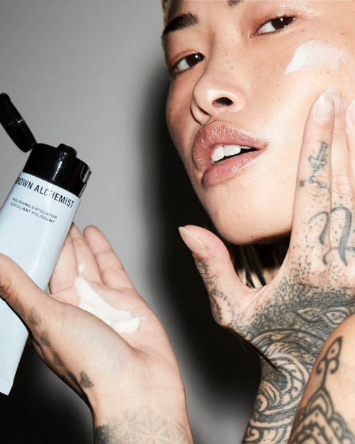 Person applying cream to face with a bottle labeled 'Grown Alchemist' in the foreground.