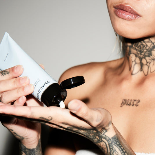 Person applying cream to their arm against a neutral background.
