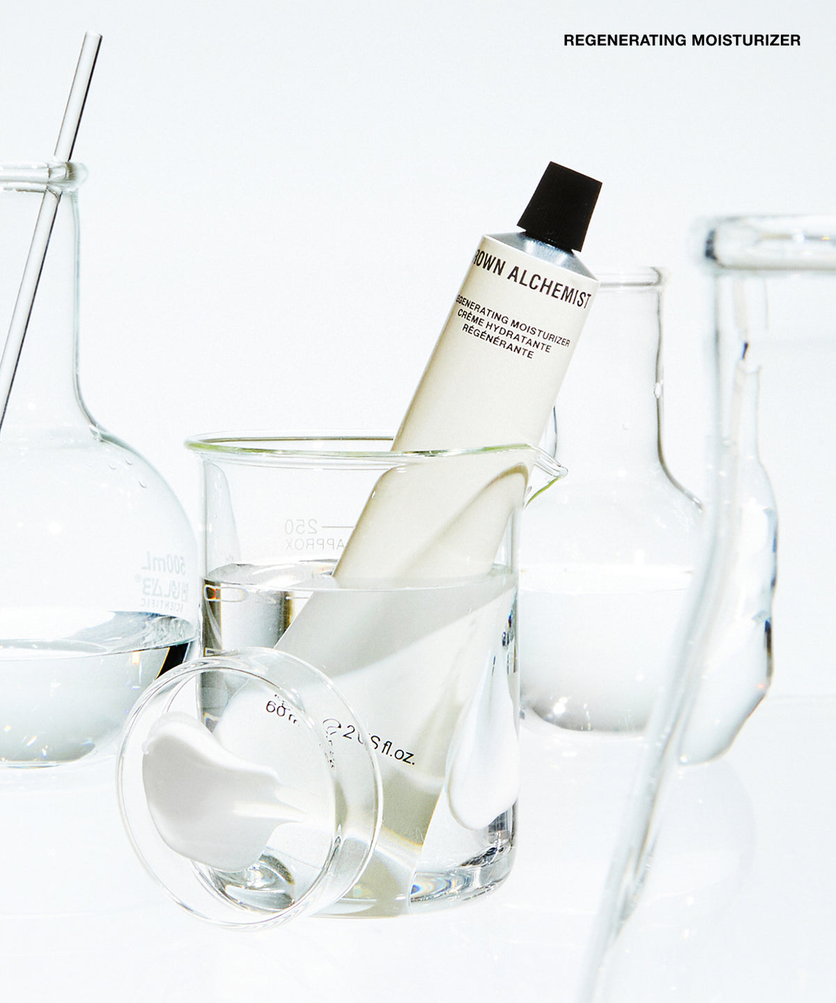 A tube of Regenerating Moisturizer standing in a glass beaker filled with liquid, surrounded by clear glass laboratory equipment on a white background.