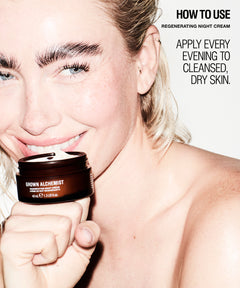 A close-up lifestyle shot of a smiling blonde woman holding a dark brown jar of GROWN ALCHEMIST Regenerating Night Cream against a clean white background with text instructions on how to use the cream.
