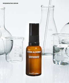 A 30ml amber glass bottle of Grown Alchemist Regenerating Serum with a black spray cap, set against a white background with blurred glass laboratory beakers.