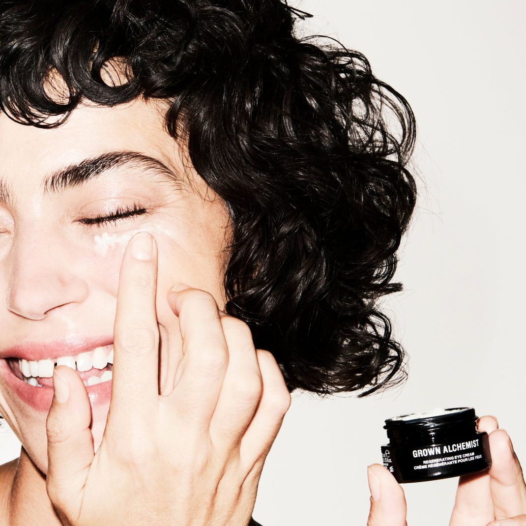 Person applying cream to face with Grown Alchemist Regenerating Eye Cream jar visible