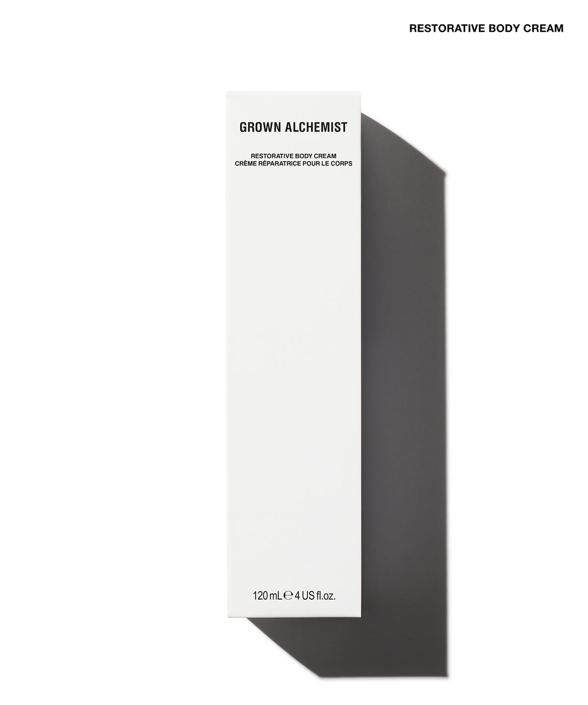 A tall, narrow white box for Grown Alchemist Restorative Body Cream, shown on a white background with a strong dark shadow to the right. The box has black text and is photographed from a top-down angle.