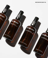 Four amber glass spray bottles of GROWN ALCHEMIST Restorative Body Oil arranged diagonally on a white background with strong shadows.
