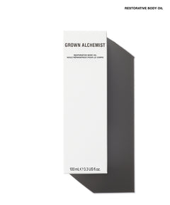 A tall, narrow white box labeled 'GROWN ALCHEMIST' and 'RESTORATIVE BODY OIL' on a white background with a dark gray cast shadow. Small text at the top right reads 'RESTORATIVE BODY OIL'.