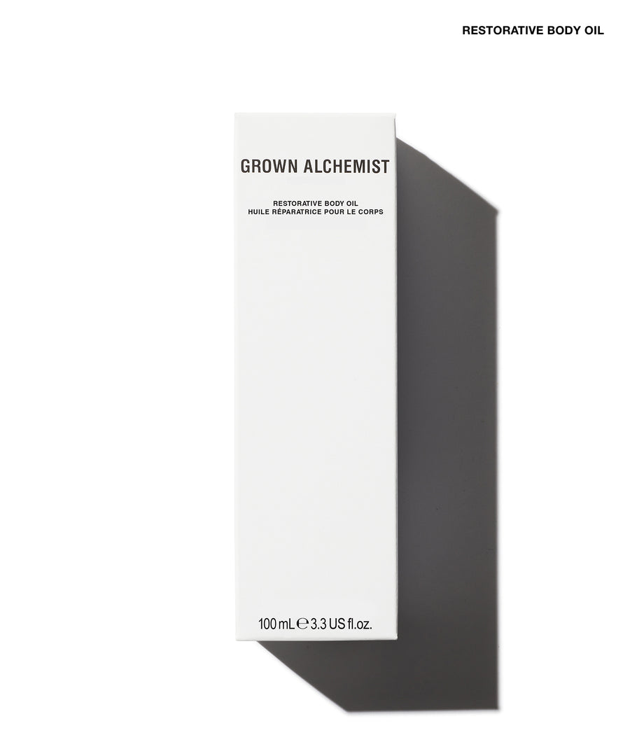 A tall, narrow white box labeled 'GROWN ALCHEMIST' and 'RESTORATIVE BODY OIL' on a white background with a dark gray cast shadow. Small text at the top right reads 'RESTORATIVE BODY OIL'.