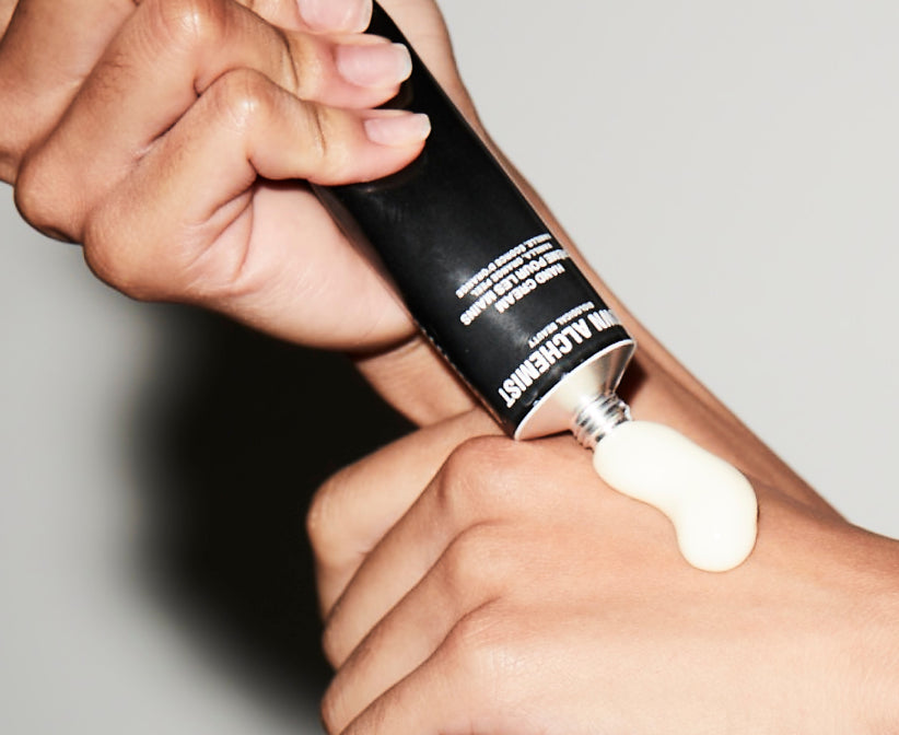 Hand applying Grown Alchemist white cream to a wrist with a black tube against a neutral background