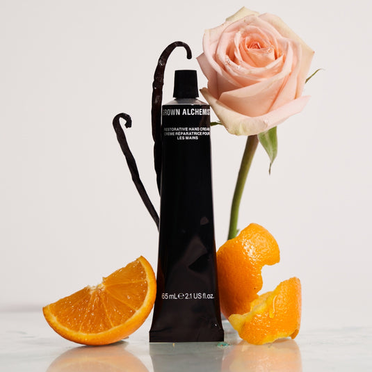 Black hand cream bottle with a pink rose and orange slices on a light background