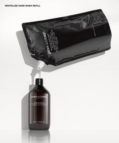 A black refill pouch labeled GROWN ALCHEMIST pouring white liquid into a dark brown bottle also labeled GROWN ALCHEMIST, on a clean white background with text reading 'REVITALIZE HAND WASH REFILL' at the top.