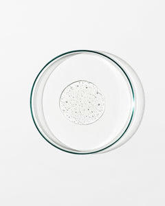 Clear glass pie dish with a dollop of liquid on a white background