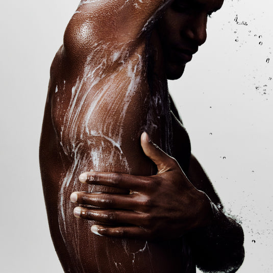 Person holding up their arm while applying  a product against a light gray background.