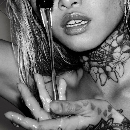 Close-up of a person with tattoos holding a mirror, with a focus on their hand and neck.