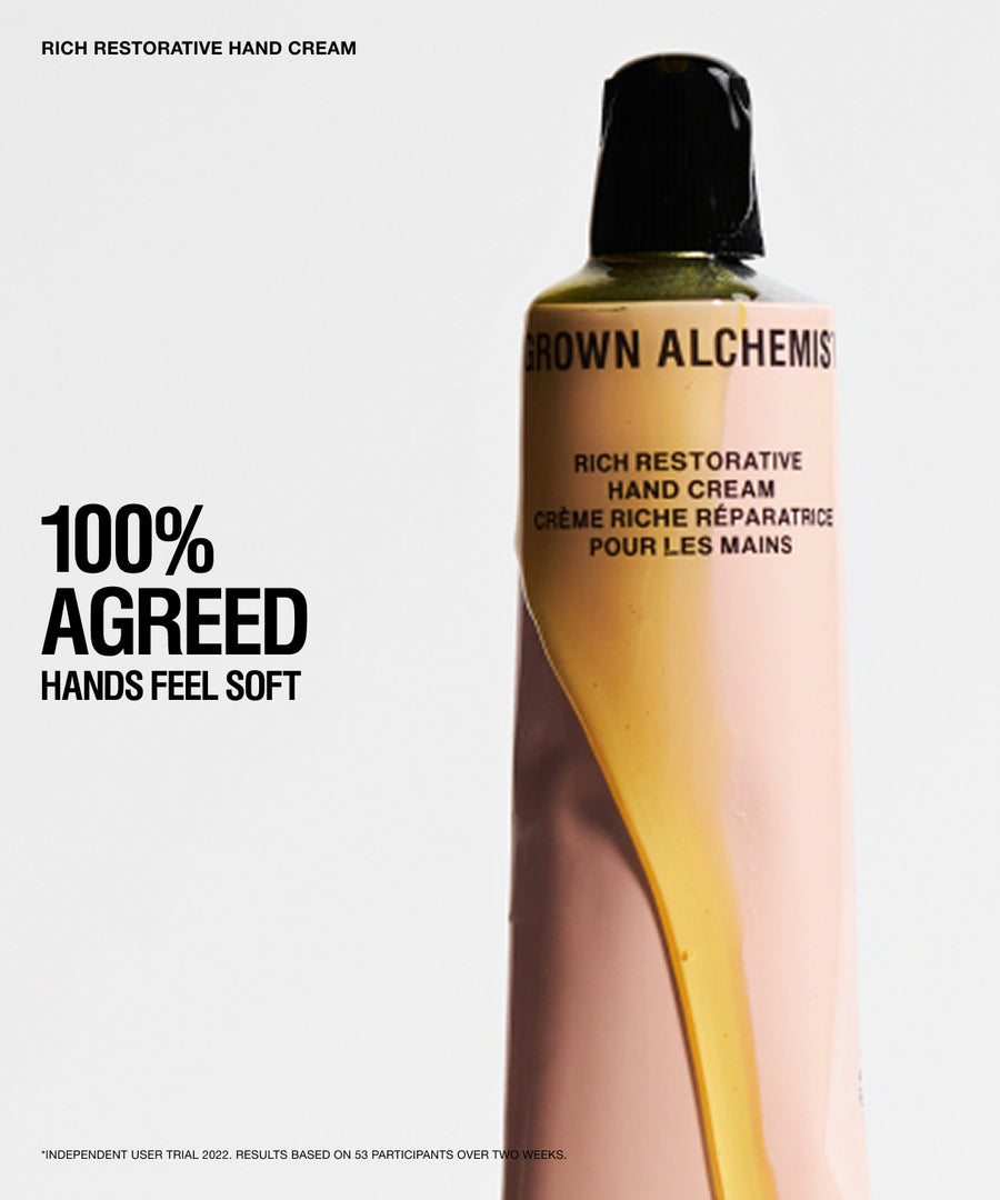 A bottle of Grown Alchemist Rich Restorative Hand Cream with a black cap, shown on a light gray background with promotional text reading '100% AGREED HANDS FEEL SOFT'.