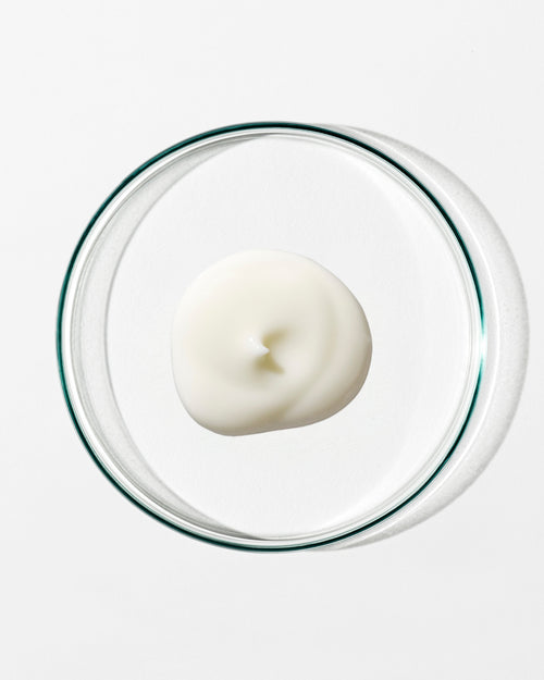 White cream in a clear glass container on a white background