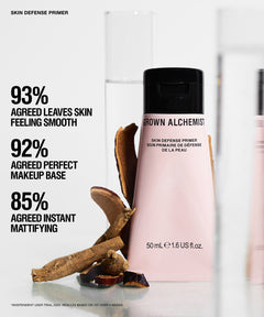Grown Alchemist Skin Defense Primer bottle in a soft pink shade with a black cap, displayed alongside natural brown botanical ingredients on a clean white background with promotional text.