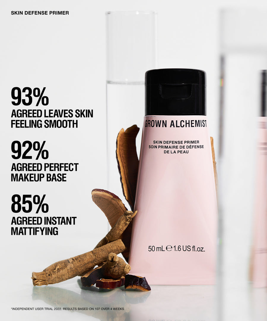 Grown Alchemist Skin Defense Primer bottle in a soft pink shade with a black cap, displayed alongside natural brown botanical ingredients on a clean white background with promotional text.