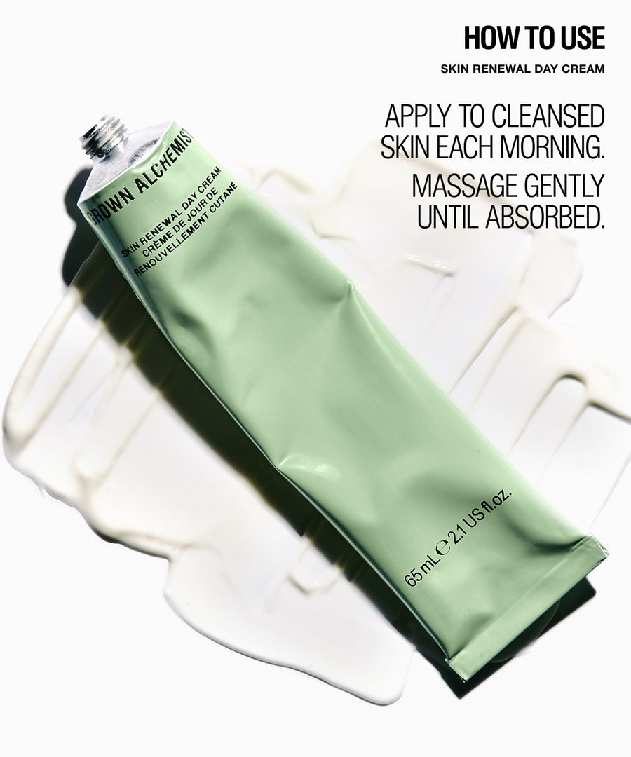 A squeeze tube of Grown Alchemist Skin Renewal Day Cream in a pale mint green color, lying diagonally on a white background with a smear of white cream underneath. Black text on the right side reads 'HOW TO USE SKIN RENEWAL DAY CREAM APPLY TO CLEANSED SKIN EACH MORNING.