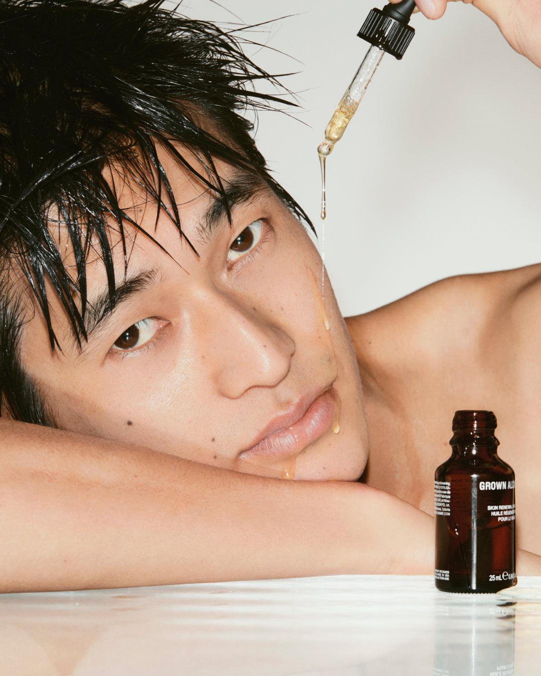 Person with dropper and bottle of skincare product on a neutral background.