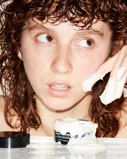 Person applying cream to face with a product on a surface