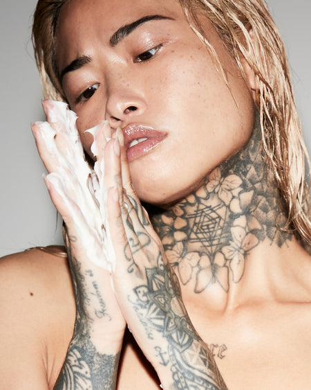 Person with tattoos on neck and hands, holding their hands near their face