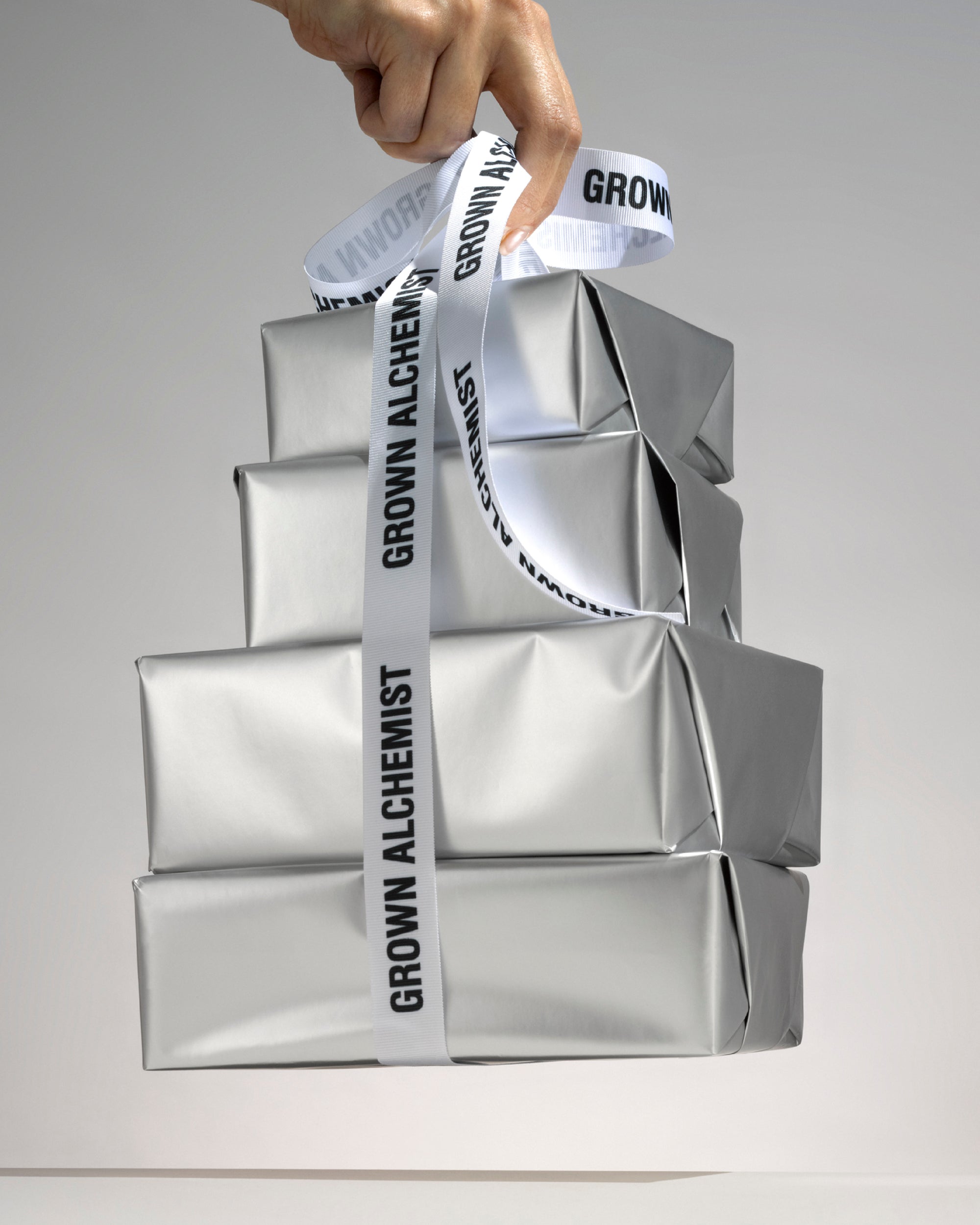 Four parcels wrapped in silver paper, bound by Grown Alchemist ribbon against a light background