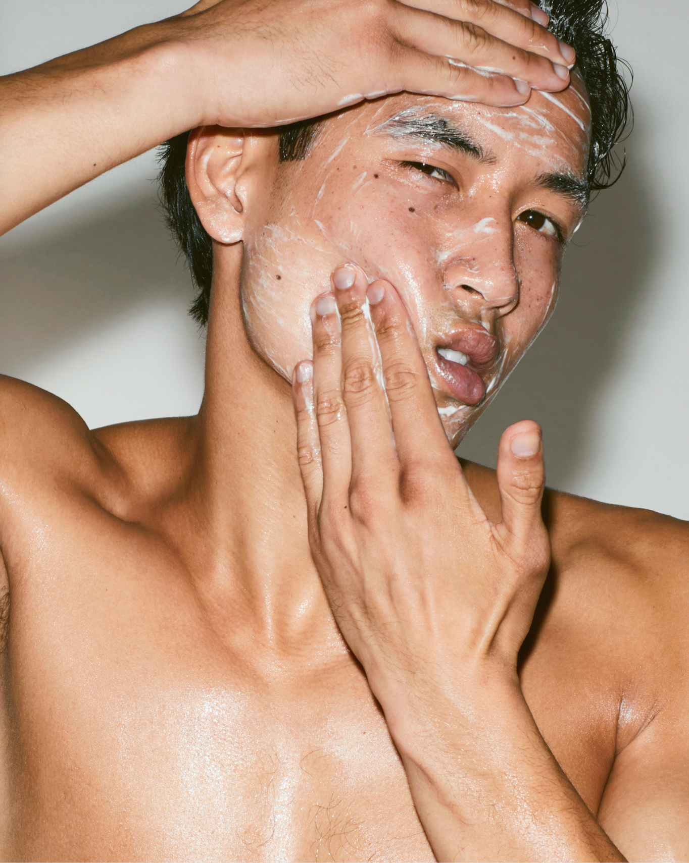 Man applying cream to his face with a neutral background
