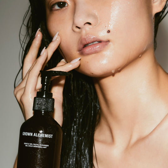 Grown Alchemist pump bottle being held by a person who is touching their face