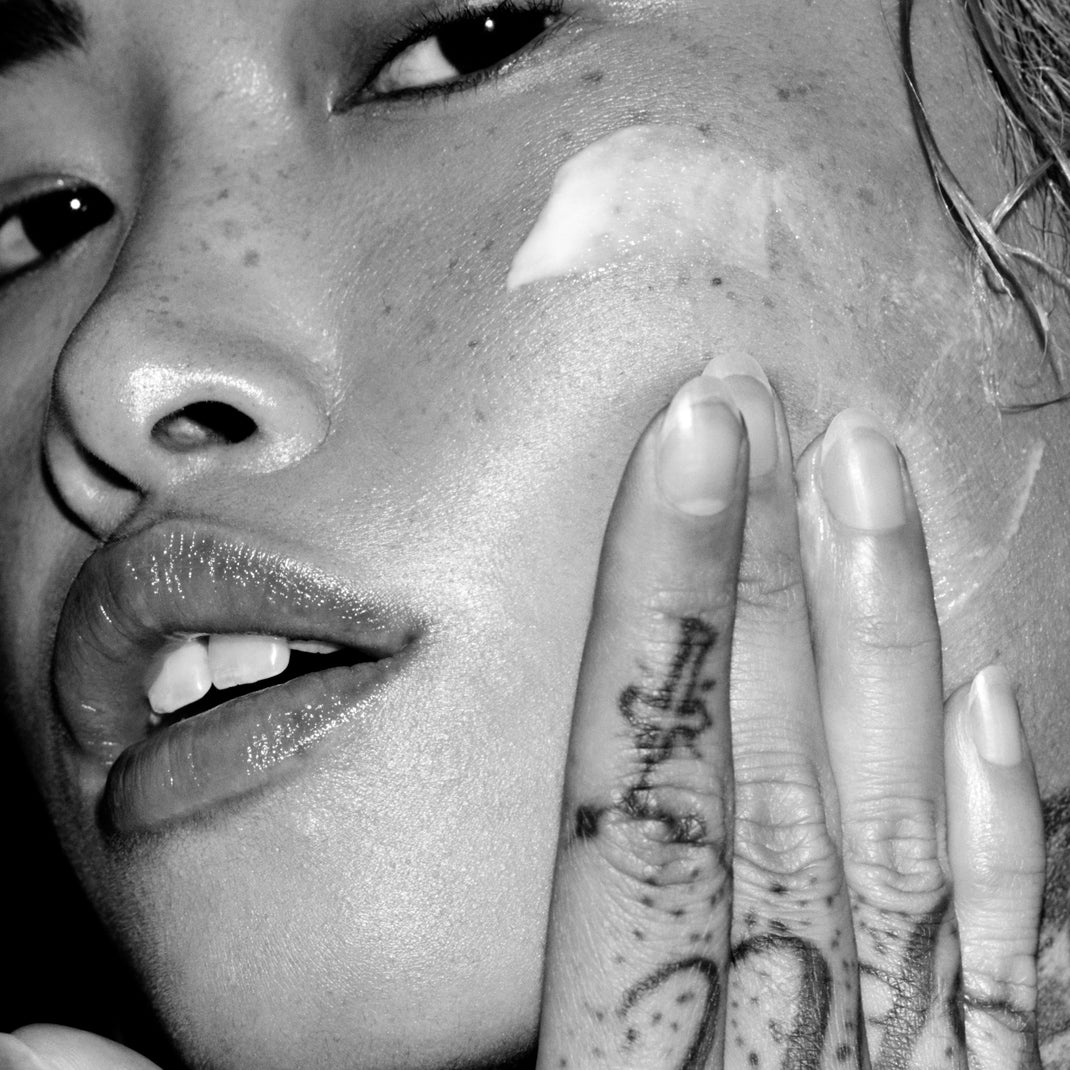 Black and white image of a person applying white cream to their face
